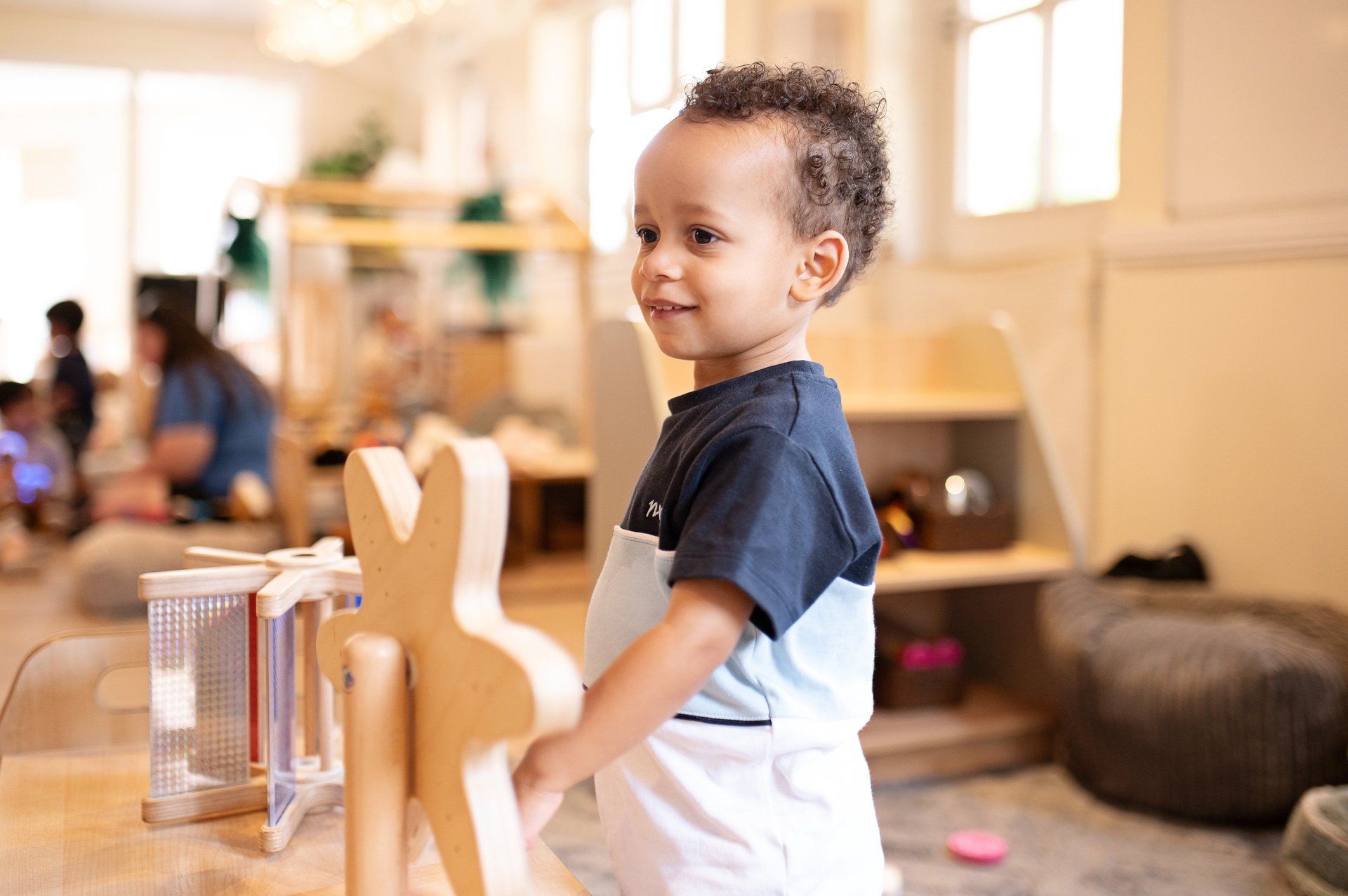 A young boy stands excitedly in front of a colourful wooden toy in a bright nursery