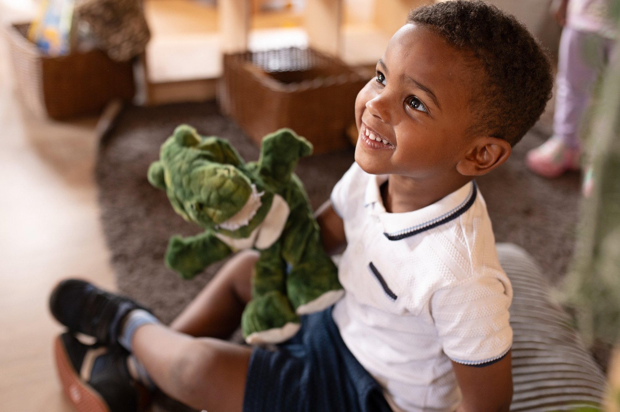 A young boy sits on the floor, happily holding a stuffed animal in a cozy nursery setting