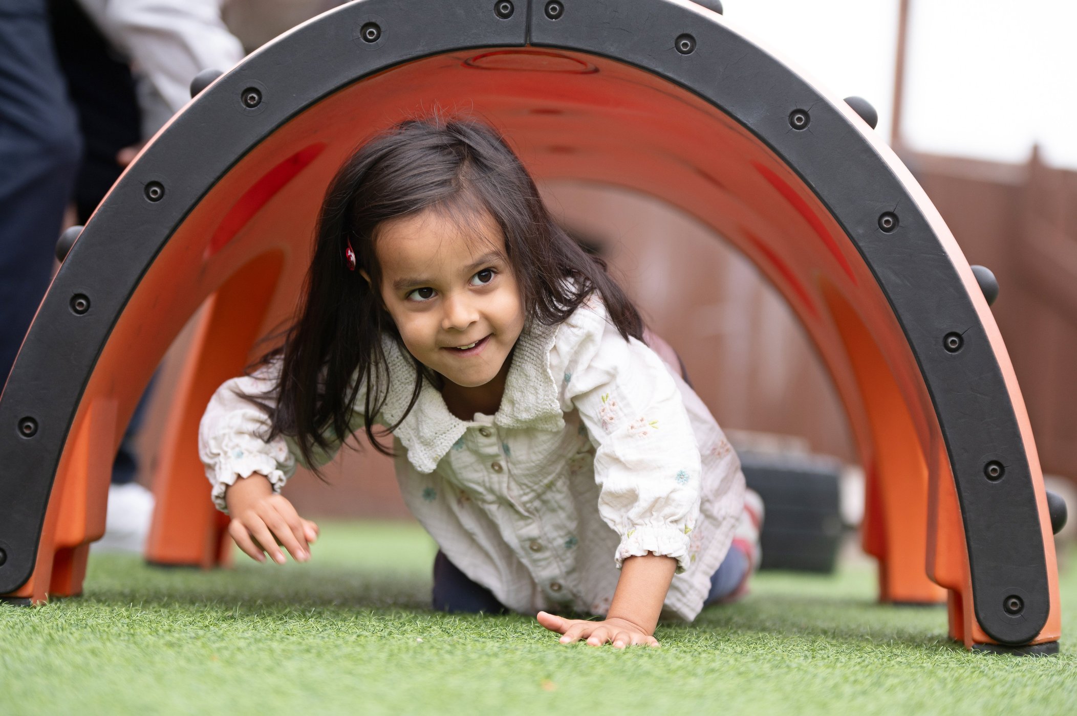 A young girl happily plays inside a colourful plastic tunnel in a nursery setting