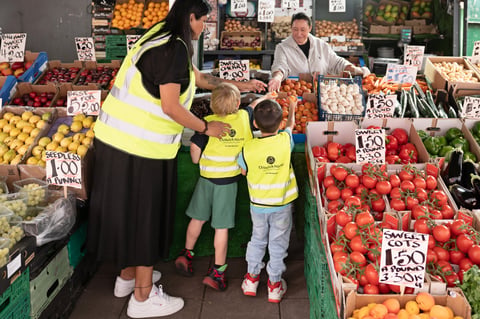 A woman and two kids browse colourful fruits and veggies at a lively market