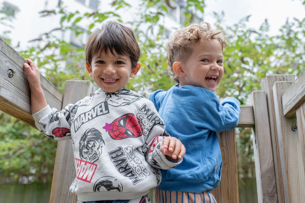 Two young boys standing on a wooden fence, smiling and enjoying their time outdoors