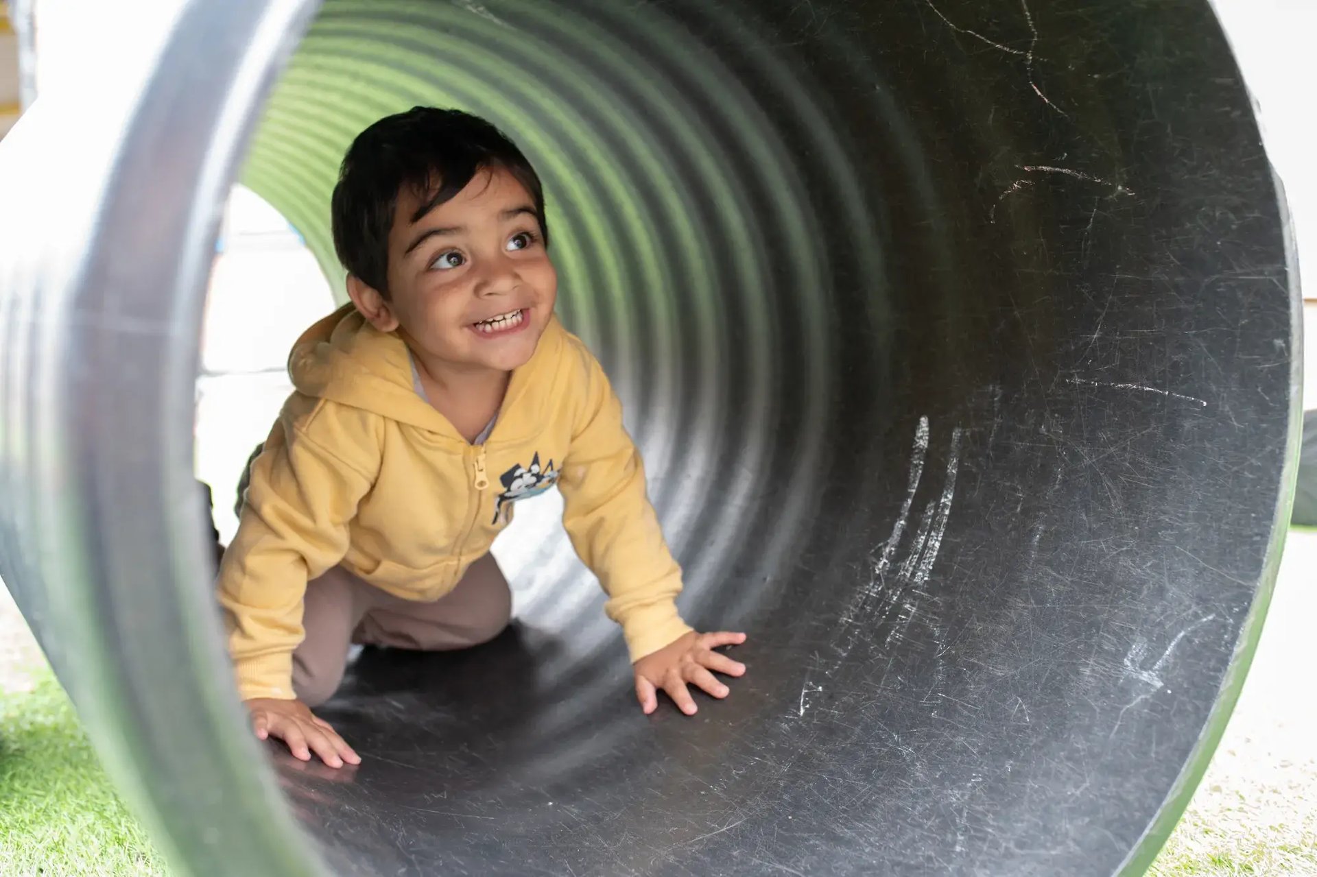 child-playing-outside-in-tunnel-at-the-kiddi-caru-day-nursery-preschool-grange-park-2000x1333
