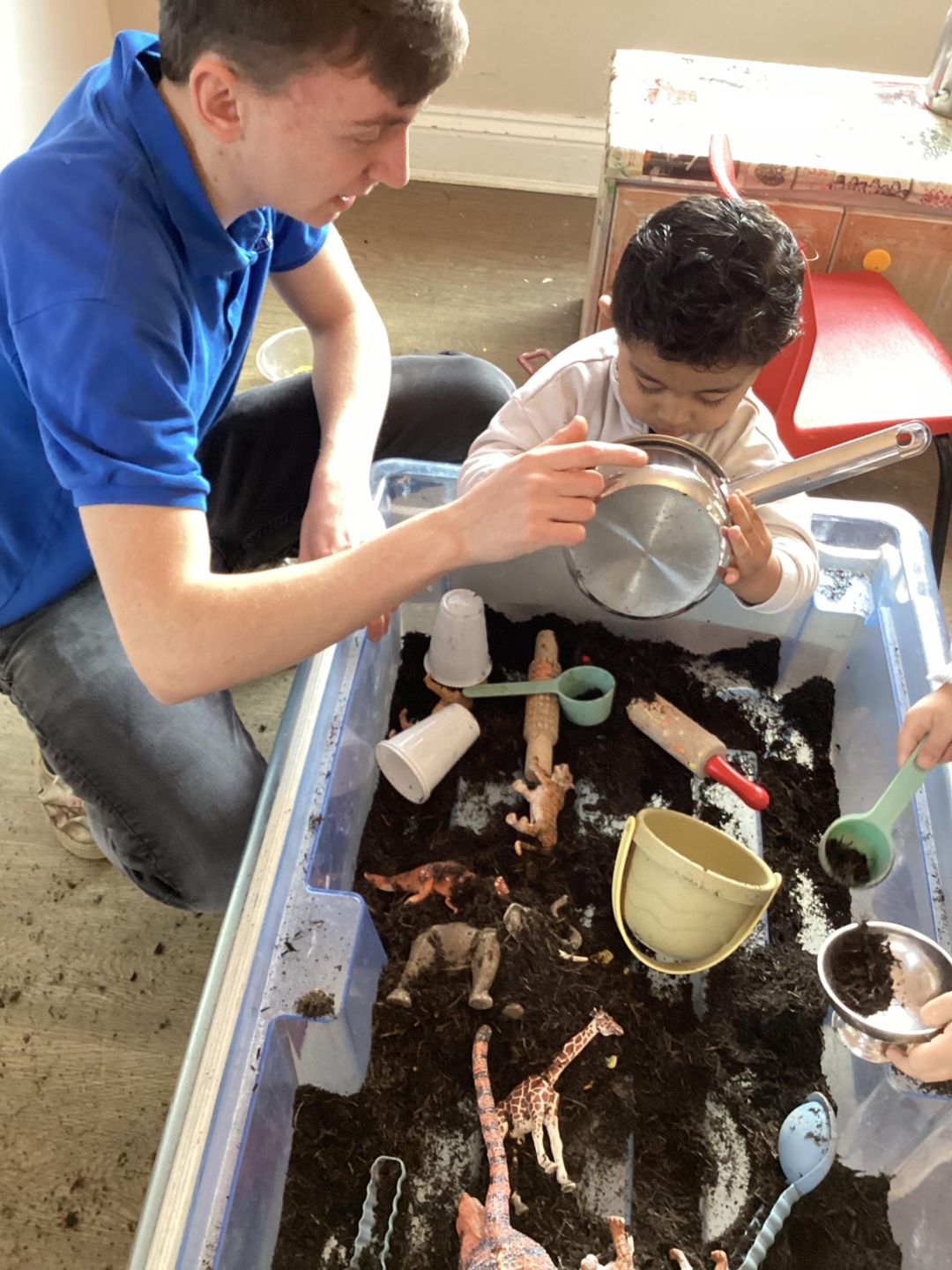 Male Nursery Practitioner helping early years child with sensory activity.