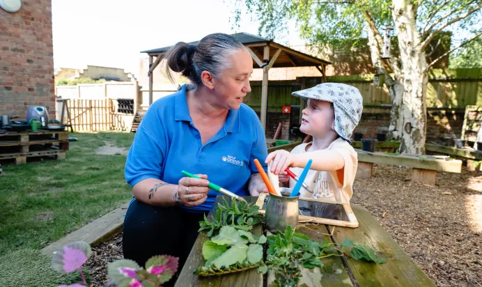 Child and key worker painting outside at Kiddi Caru Day Nursery Preschool Leighton Buzzard