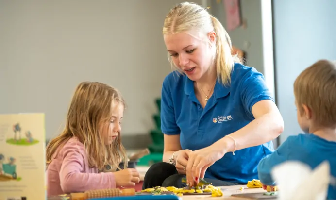 Child and key worker play with dinosaur toys at Kiddi Caru Day Nursery Preschool Market Harborough