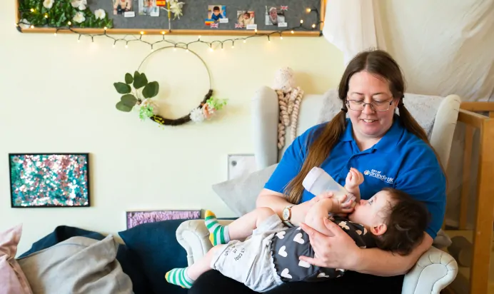 Child being fed a bottle by key worker at Kiddi Caru Day Nursery Preschool Leighton Buzzard