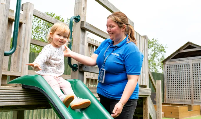 Child being helped down slide by key worker at Kiddi Caru Day Nursery Preschool Market Harborough