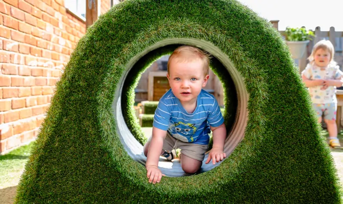 Child crawling through grass tunnel at Kiddi Caru Day Nursery Preschool Leighton Buzzard