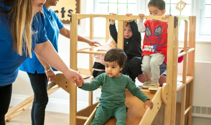 Child going down the slide with help of key workers at Little Acorns Day Nursery Preschool Stoneygate