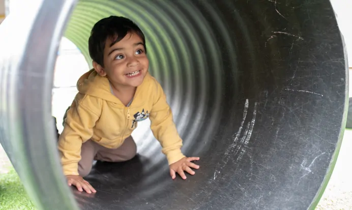 Child playing outside in tunnel at The Kiddi Caru Day Nursery Preschool Grange Park