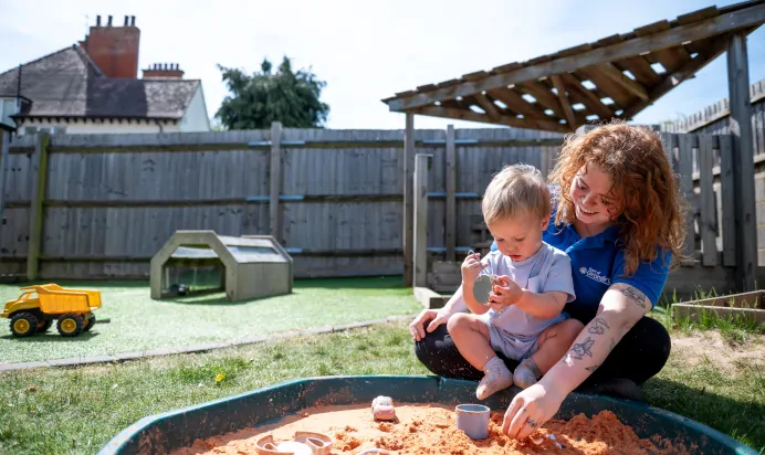 Child playing with key worker outside in sandpit at Kiddi Caru Day Nursery Preschool Abington Park Northampton