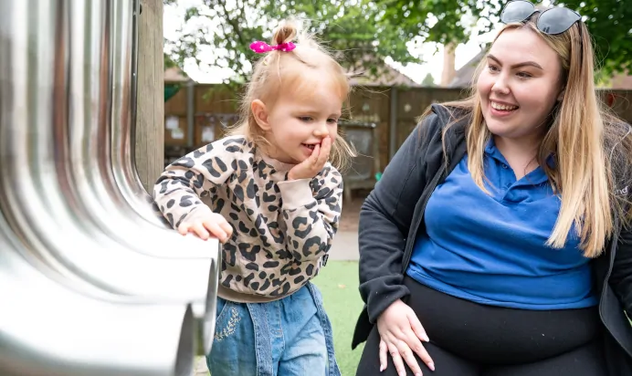Child playing with musical instrument outdoors with key worker at Little Acorns Day Nursery Preschool Stoneygate