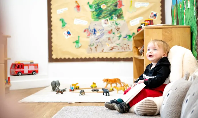 Child sitting in book corner holding a book at Kiddi Caru Day Nursery Preschool Plympton Plymouth