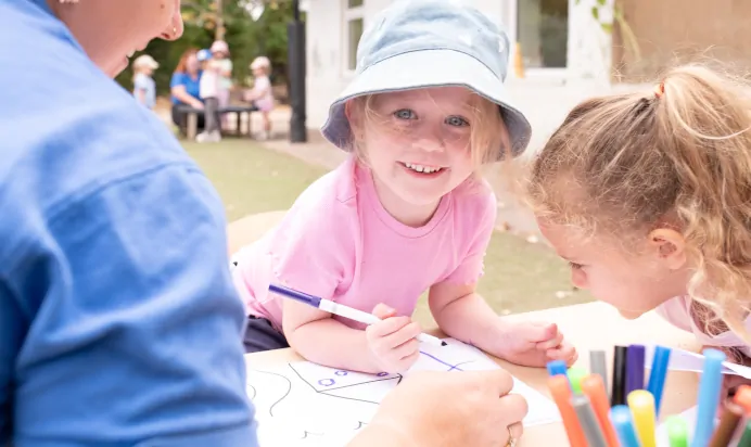 Child smiling and colouring at The Kiddi Caru Day Nursery Preschool Writtle