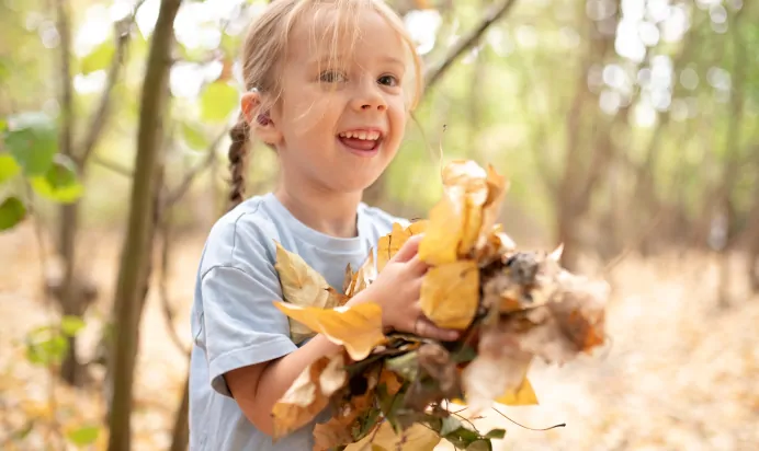 Child smiling while holding leaves at The Kiddi Caru Day Nursery Preschool Writtle