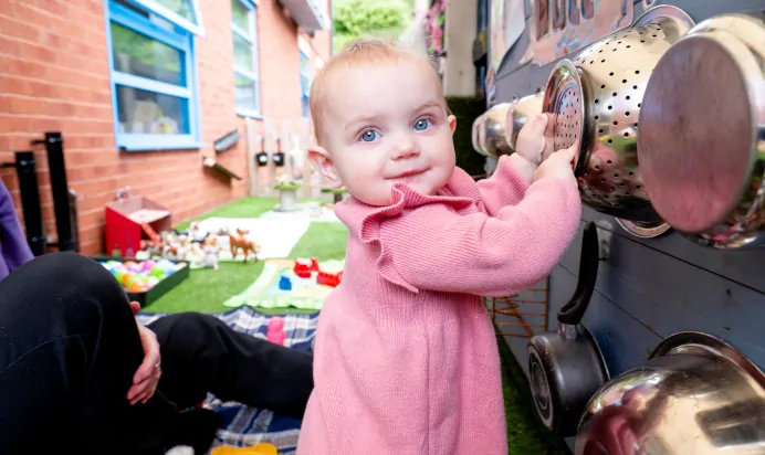 Child smiling while playing with musical playing equipment at Kiddi Caru Day Nursery Preschool Torquay