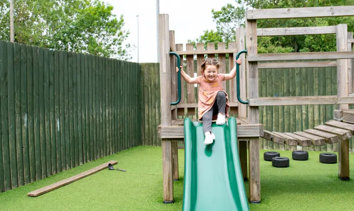 Child smiling whilst going down slide at Kiddi Caru Day Nursery Preschool Market Harborough