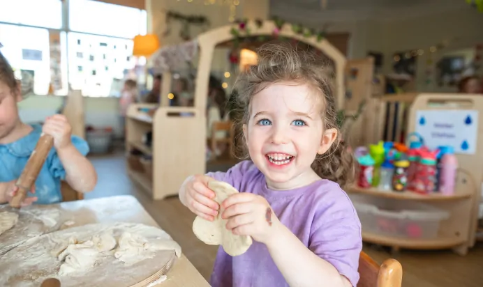 Child smiling whilst making dough at Kiddi Caru Day Nursery Preschool Leighton Buzzard