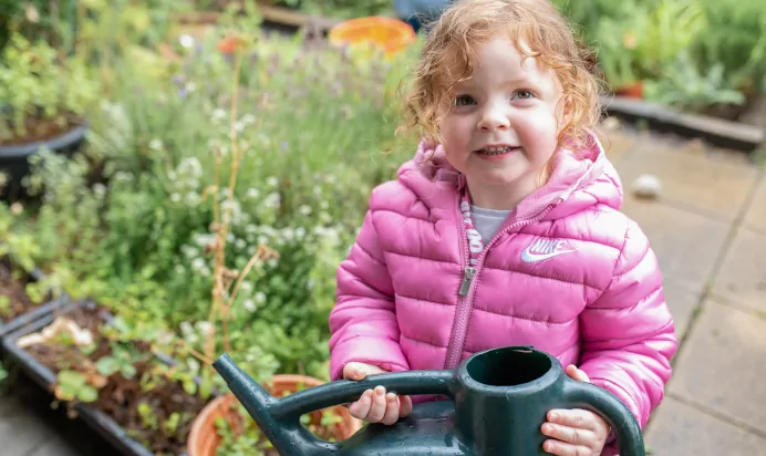 Child smiling with watering can at The Kiddi Caru Day Nursery Preschool Burgess Hill