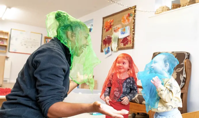 Children and key worker playing with colourful netting at Charnwood Day Nursery Preschool Shepshed Loughborough