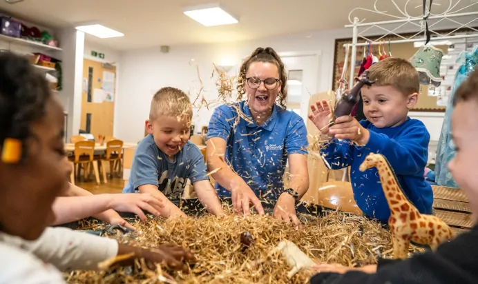 Children and key worker playing with straw and toy animals at Kiddi Caru Day Nursery Preschool Peterborough