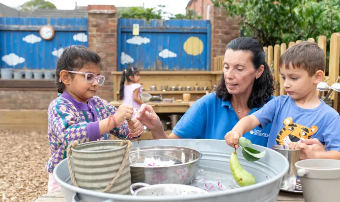 Children collaborating in outside space with key worker at The Kiddi Caru Day Nursery Preschool Grange Park