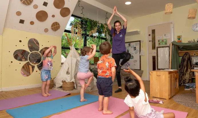 Children doing yoga poses with key worker at Kiddi Caru Day Nursery Preschool Whiteley