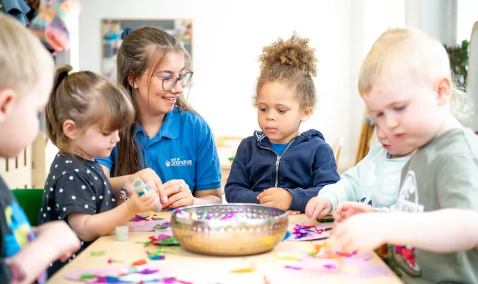 Children gluing art together with key worker at The Laurels Day Nursery Preschool Queniborough