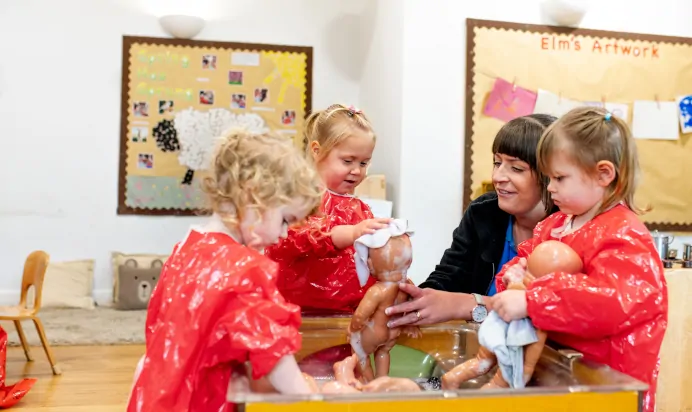 Children in aprons washing toy babies with key worker at Kiddi Caru Day Nursery Preschool Plympton Plymouth