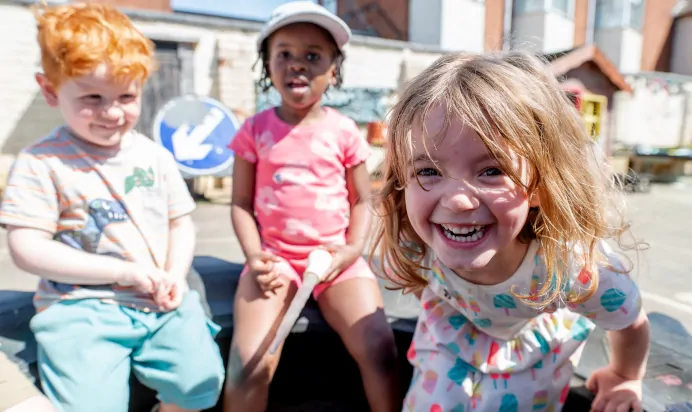 Children outside smiling to the camera in a tyre at Kiddi Caru Day Nursery Preschool Abington Park Northampton