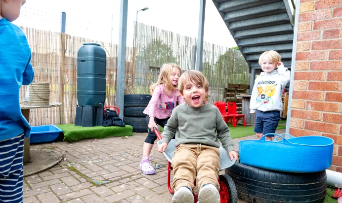 Children play with wheelbarrow in the garden at Kiddi Caru Day Nursery Preschool Market Harborough