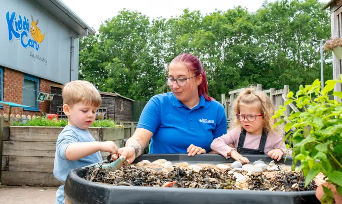 Children playing in sand pit outside with shells and stones at Kiddi Caru Day Nursery Preschool Market Harborough