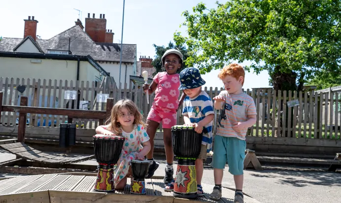 Children playing musical instruments outdoors at Kiddi Caru Day Nursery Preschool Abington Park Northampton