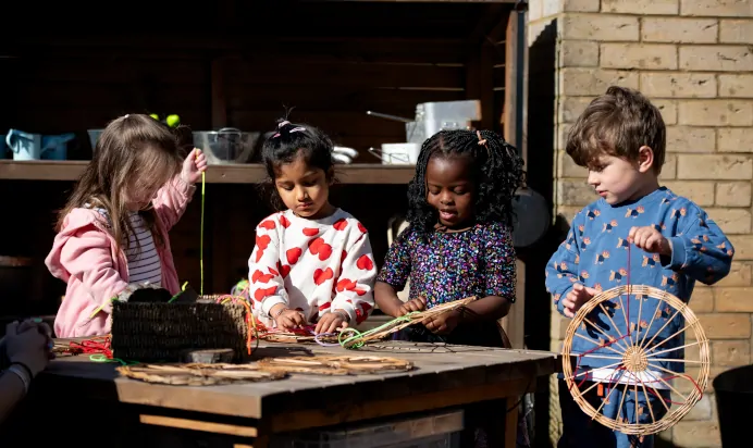 Children playing outdoors together with wood and string at Kiddi Caru Day Nursery Preschool Caldecotte Milton Keynes