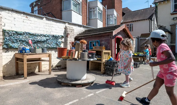 Children playing outside together in the sun at Kiddi Caru Day Nursery Preschool Abington Park Northampton