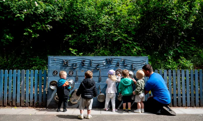 Children playing outside with music playing equipment at Kiddi Caru Day Nursery Preschool Torquay