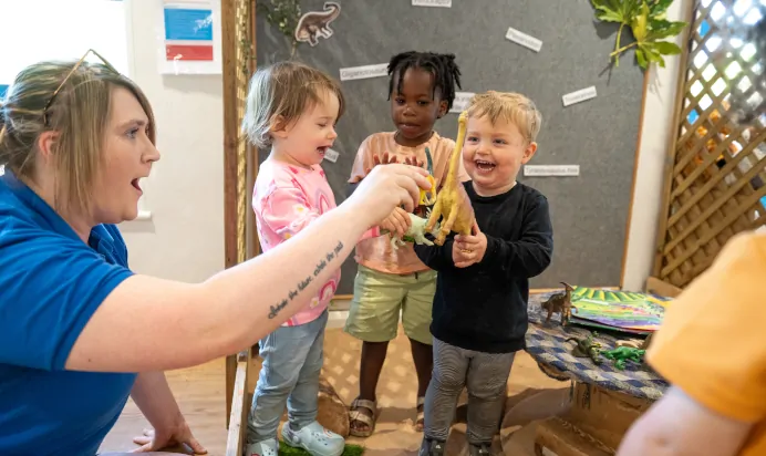 Children playing with dinosaur toys and key worker at Kiddi Caru Day Nursery Preschool Wellingborough
