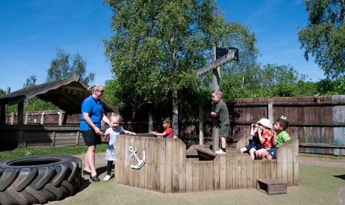 Children playing with key worker in wooden pirate ship at Kiddi Caru Day Nursery Preschool Wellingborough