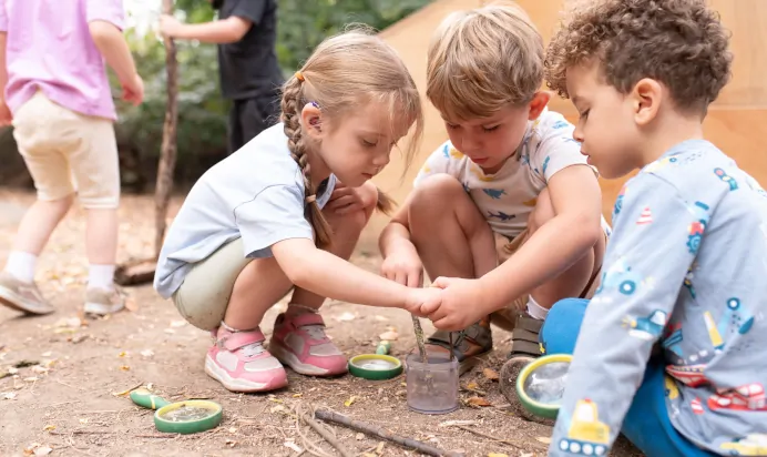 Children playing with magnifying glasses and sticks at The Kiddi Caru Day Nursery Preschool Writtle