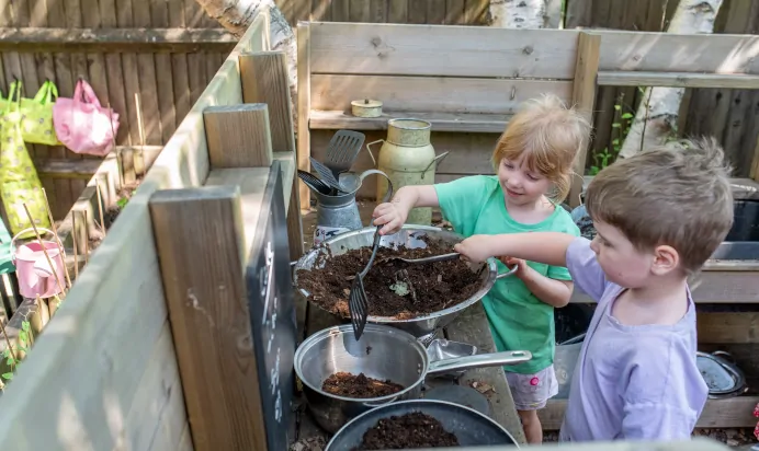 Children pretending to cook in play kitchen outside at Kiddi Caru Day Nursery Preschool Whiteley