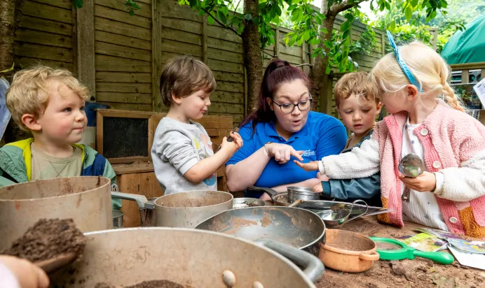 Children searching through dirt in interactive outdoor space with key worker at Kiddi Caru Day Nursery Preschool Torquay