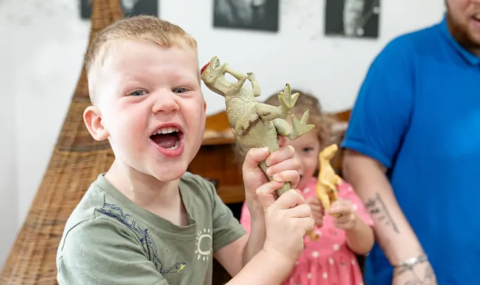 Children smiling with toy dinosaur at The Kiddi Caru Day Nursery Preschool Burgess Hill