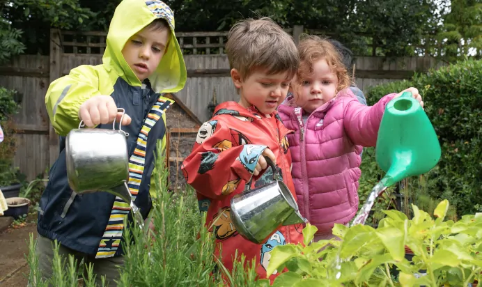 Children watering plants outside together at The Kiddi Caru Day Nursery Preschool Burgess Hill