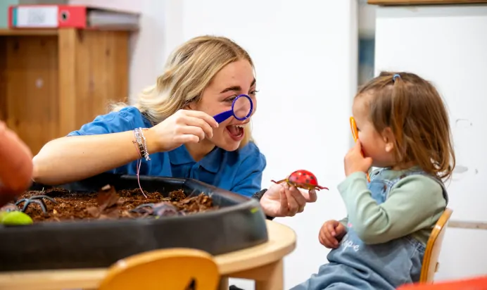 Key worker and child looking through magnifying glasses at Kiddi Caru Day Nursery Preschool Plympton Plymouth