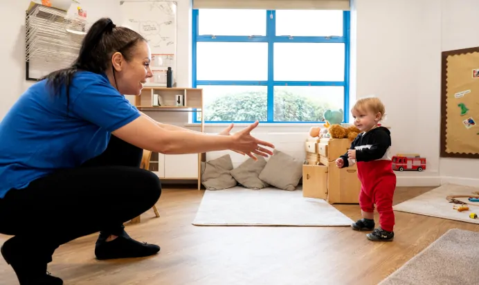 Key worker encouraging child to walk to her at Kiddi Caru Day Nursery Preschool Plympton Plymouth