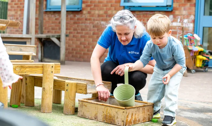 Key worker helping child fill up plant pot with water at Kiddi Caru Day Nursery Preschool Market Harborough
