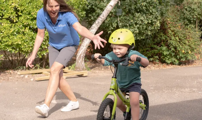 Key worker helping child ride bicycle at The Kiddi Caru Day Nursery Preschool Writtle