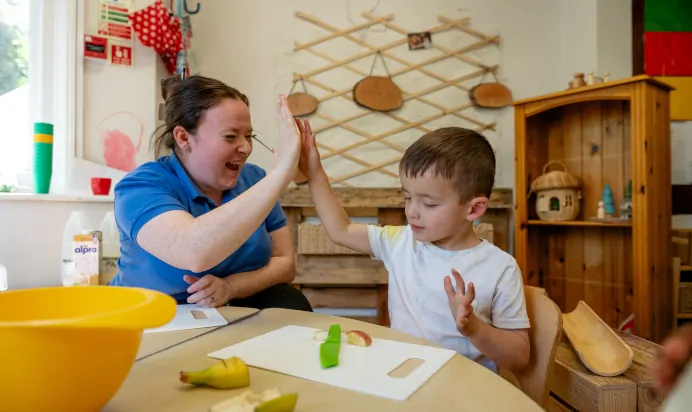 Key worker high fives child for cutting apple at Kiddi Caru Day Nursery Preschool Abington Park Northampton