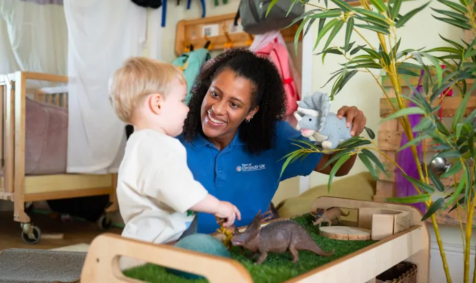 Key worker playing with dinosaurs with child at Kiddi Caru Day Nursery Preschool Leighton Buzzard