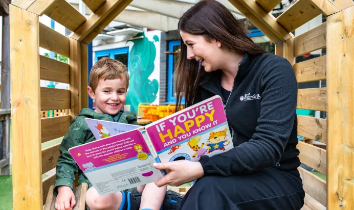 Key worker reading book to child outside at Kiddi Caru Day Nursery Preschool Peterborough